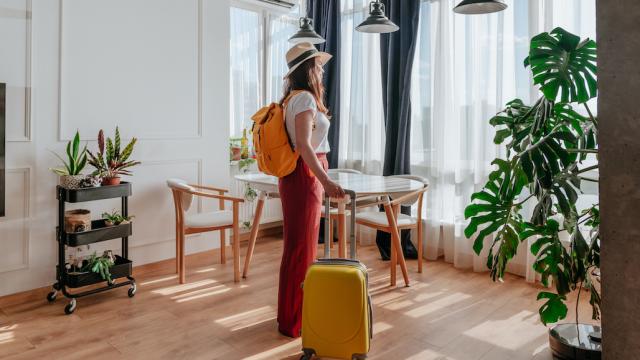 A tourist with her luggage stands in the middle of her accommodation.